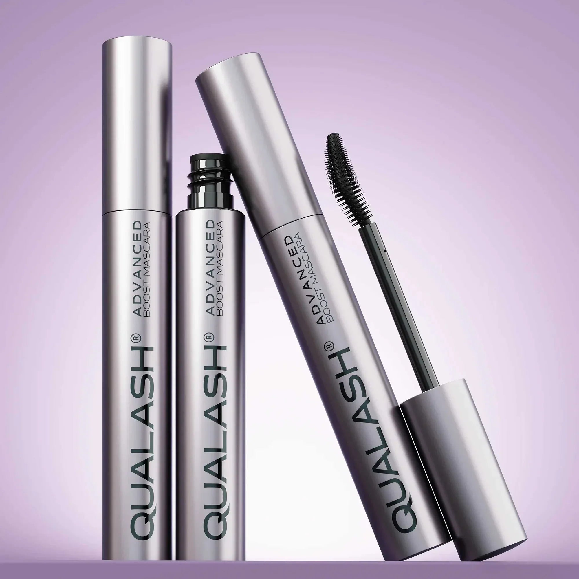 Multiple QUALASH Curl & Lift mascaras arranged creatively on soft purple background with focus on brush and tube