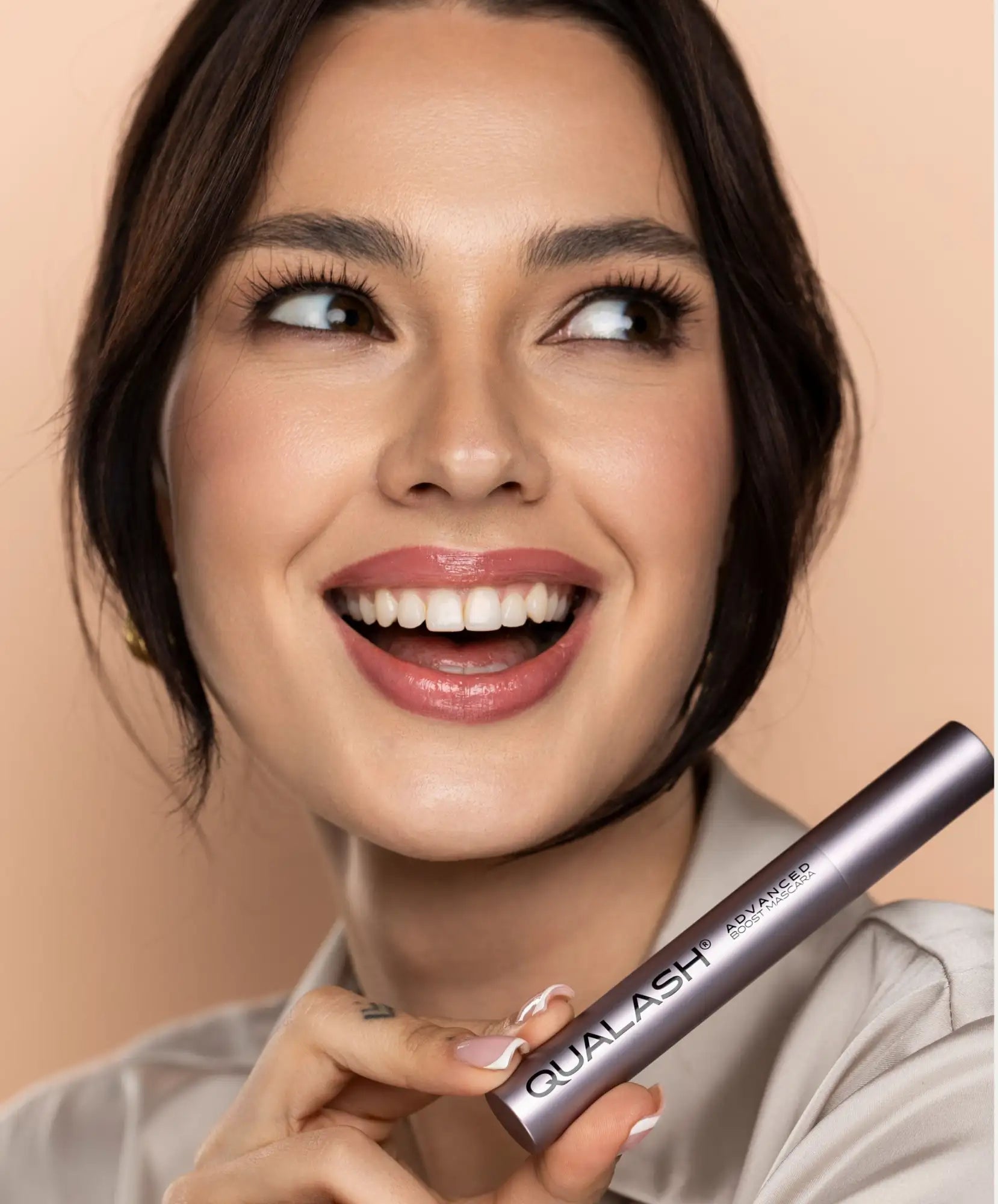 A sleek, metallic silver mascara tube with the brand name ’qualash’ and product line ’advanced’ printed in white lettering.